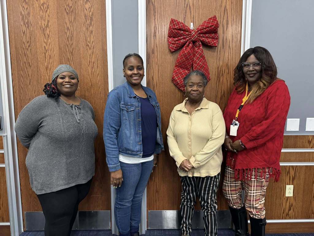 Four School Board Directors are standing in front of a wooden door adorned with a large red bow.