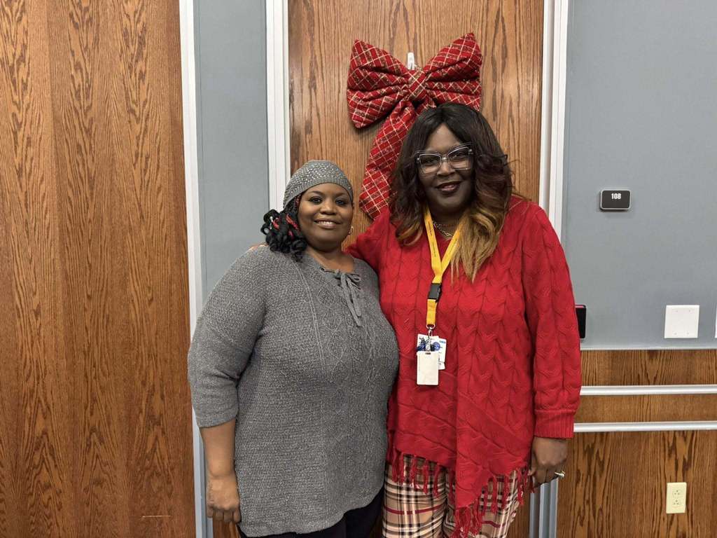 Two School Board Directors are standing in front of a wooden door adorned with a large red bow.