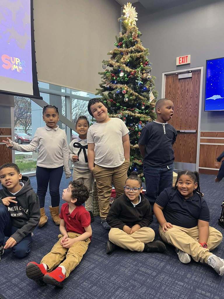 A group of eight children are gathered in front of a decorated Christmas tree.