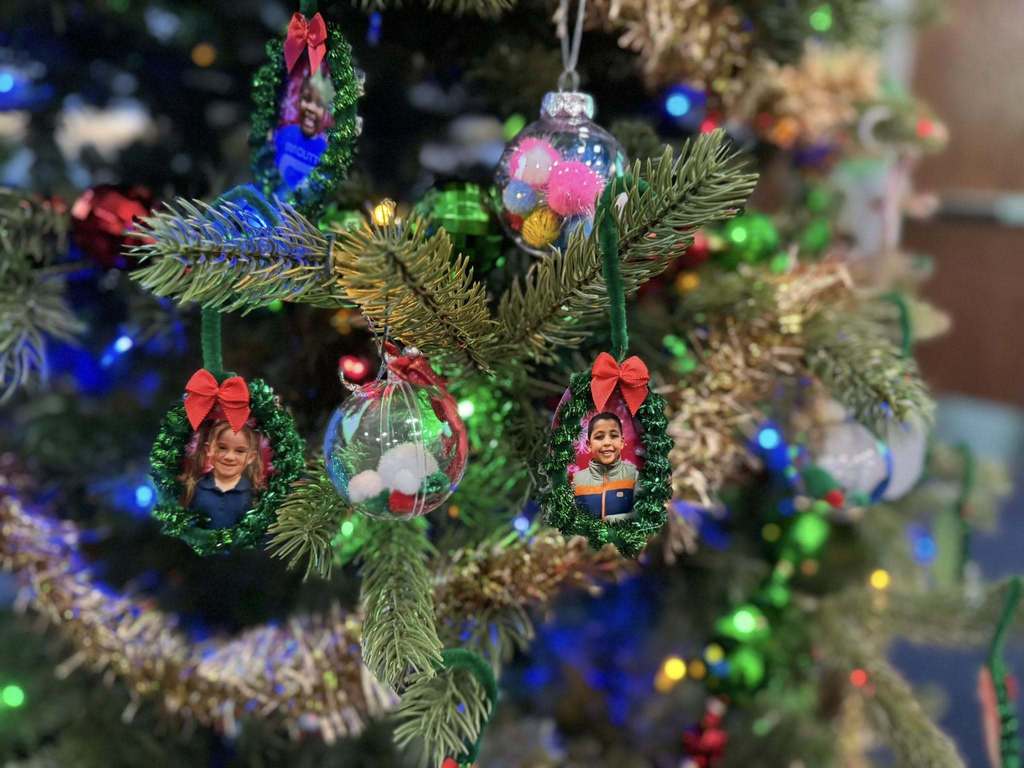 A decorated Christmas tree with colorful lights and ornaments. Decorations include photo frames with red bows, filled baubles, and tinsel.