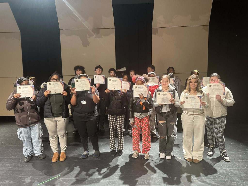 A group of students are standing on stage, holding certificates.