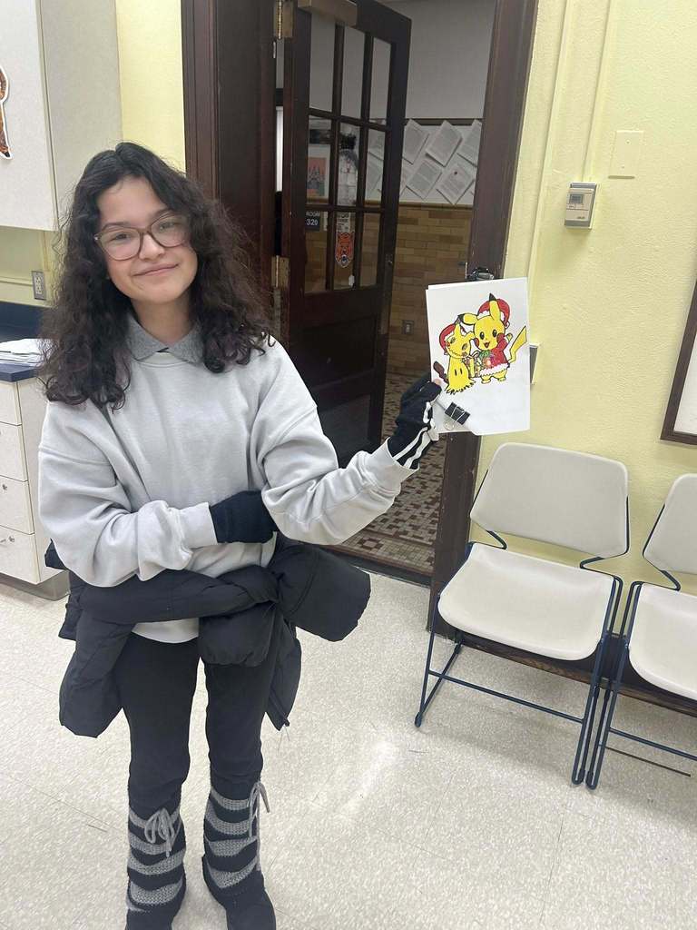 A student is standing in a school classroom, holding up a colorful drawing of two cartoon characters.