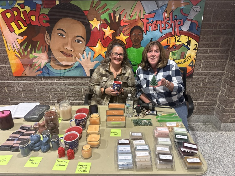 Two district staff members are holding up candles while a table full of candles is in front of them.