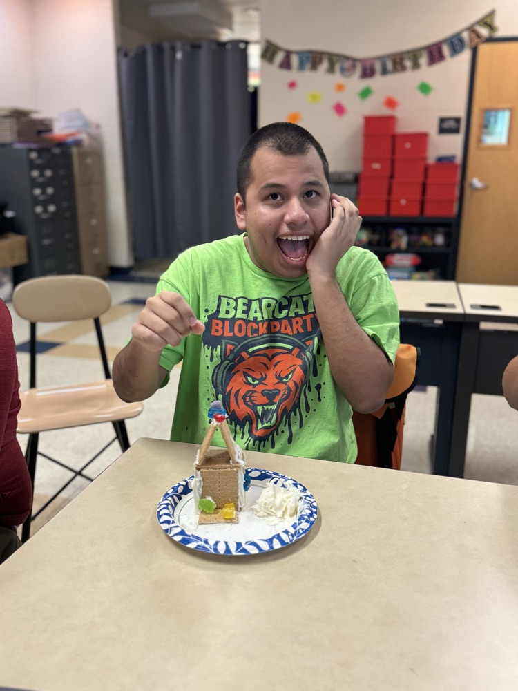 A student is sitting at a desk with a gingerbread house in front of him.