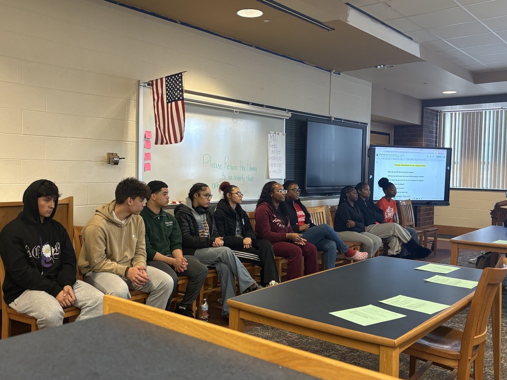 A group of William Penn Senior High School alumni students are sitting in front of a whiteboard in a row in a school library.