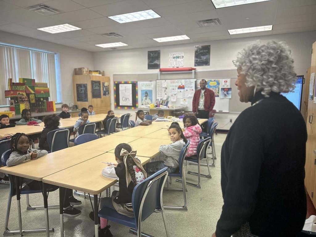 Representative Carol Hill-Evans is speaking to a group of students who are sitting at tables in a school classroom. A district staff member can be seen standing nearby.