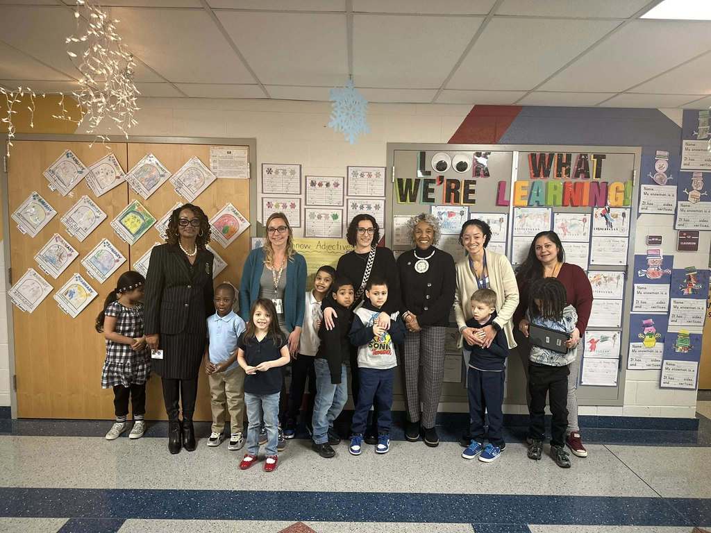 A group of students, district administration, district staff members and Representative Carol Hill-Evans are standing in a school hallway in front of colorful bulletin boards with student artwork and the words "Look What We're Learning" displayed on them.