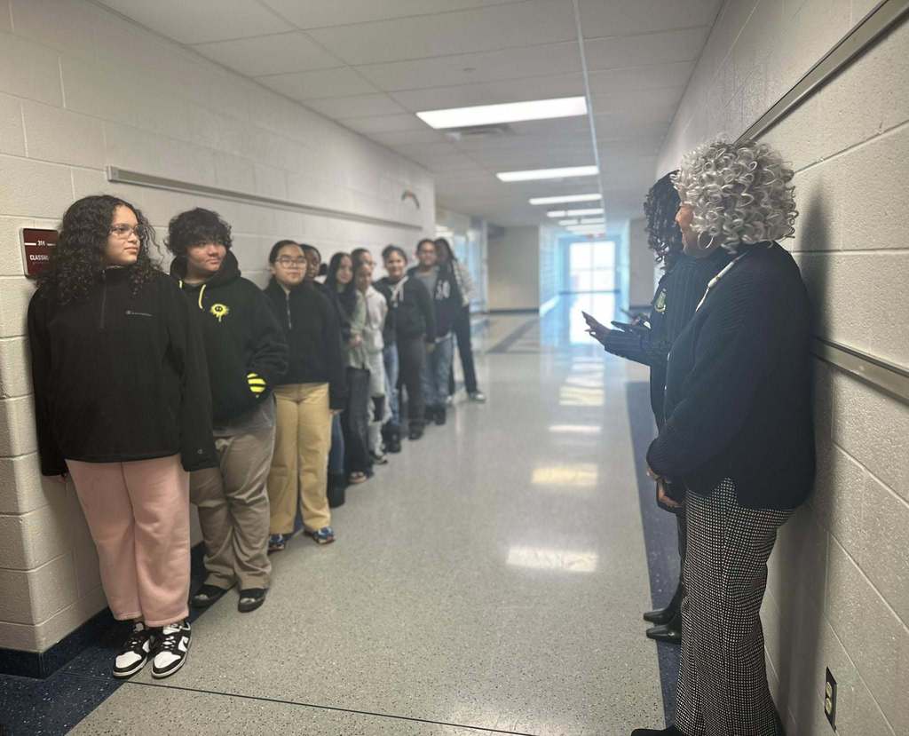 A group of students are standing in a line in a school hallway, facing district administration and Representative Carol Hill-Evans.