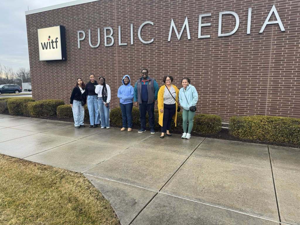 A group of seven people, including district staff members and students are standing in front of a building labeled "witf PUBLIC MEDIA."