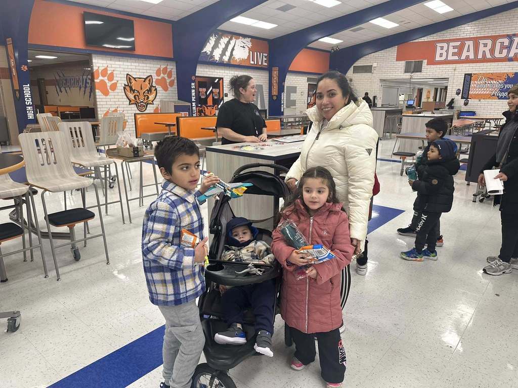 A family, including a child in a stroller and two kids holding snacks, are standing in a school cafeteria decorated with orange and blue Bearcats logos.