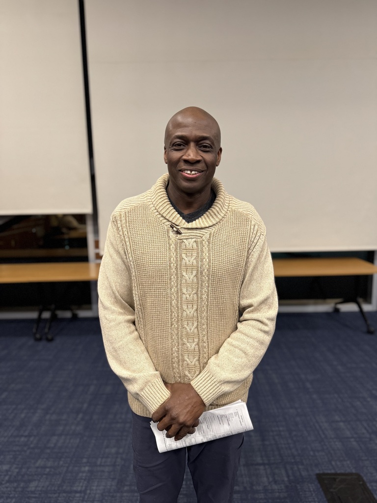 The School District of the City of York's newest School Board Director, Halman Smith II, standing in a conference room holding a paper in both of his hands. A table and screens can be seen in the background.