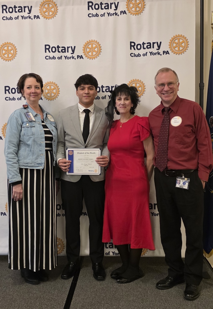 Three district staff members and one student are standing in front of a Rotary Club of York, PA backdrop. The student is holding a certificate in his hand.