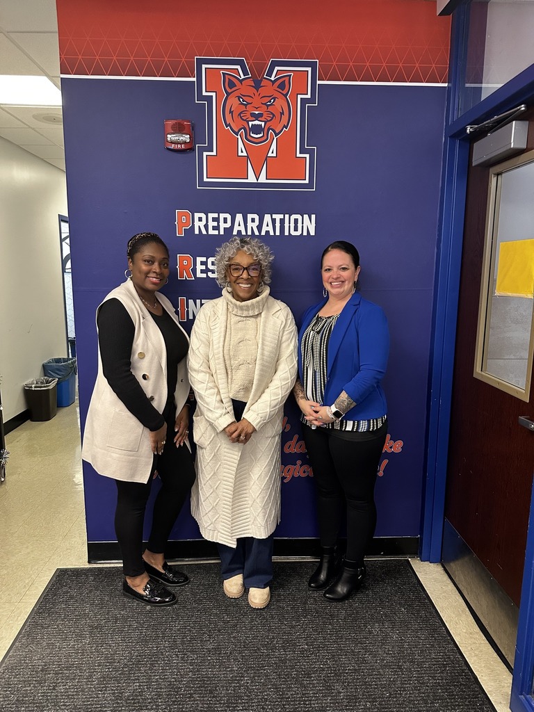 McKinley PreK-8 Administration and Representative Carol Hill-Evans are standing in an office area in front of a school-themed wall with a bear and words that say "Preparation" and "Respect." 