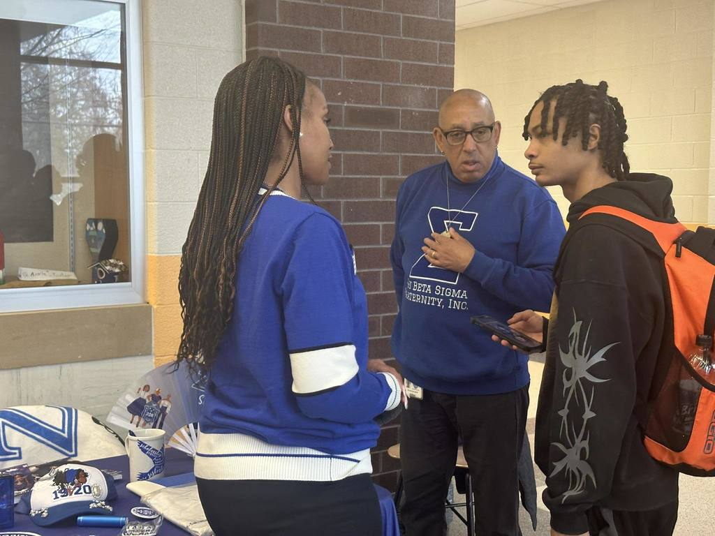 A woman and a district staff member are having a discussion with a student in a school hallway. 