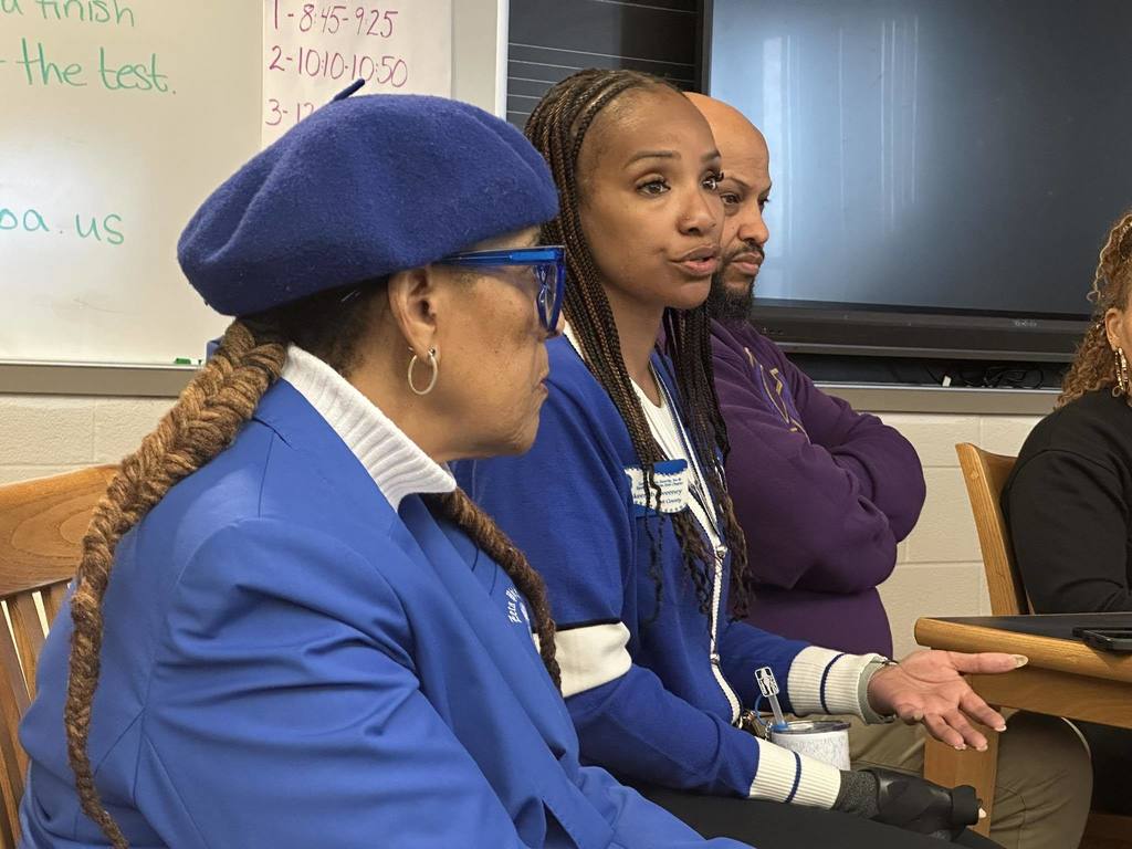 Two women and a district administrator are sitting around a table in a school library, engaging in a discussion.