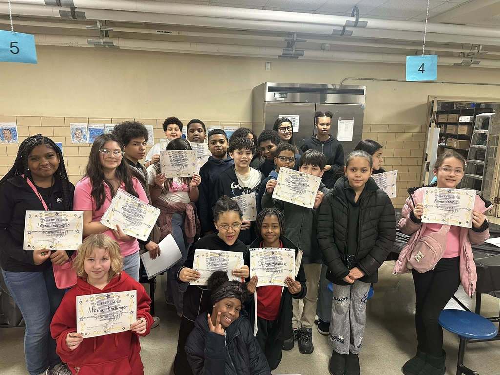 A group of students are standing and kneeling down in a school cafeteria while holding certificates in their hands.