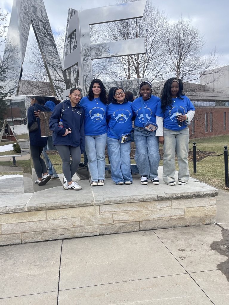 Five students are standing on a stone platform in front of large silver letters. 