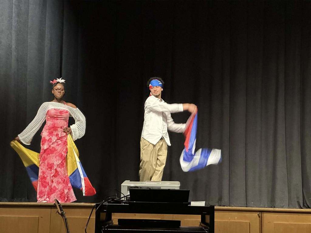 Two students are walking across a stage holding flags. 