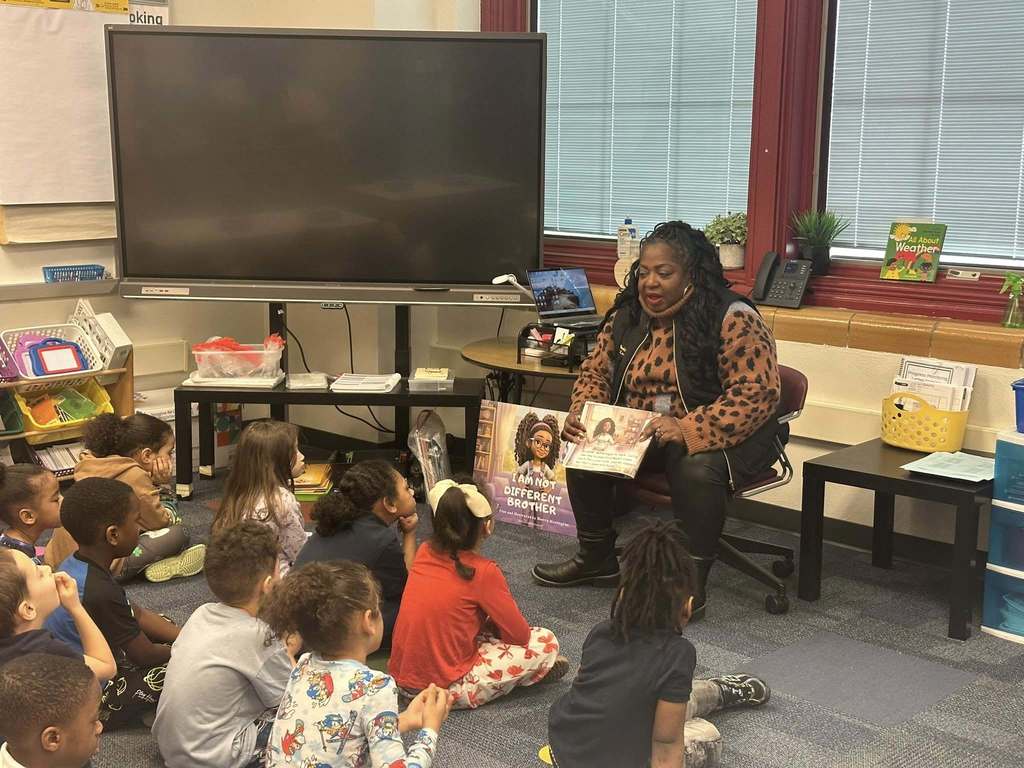 Local community member and author, Dr. Sherry Washington, is reading to a classroom of students who are sitting on a carpet.