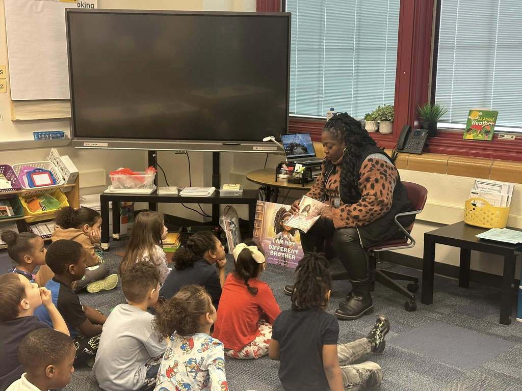 Local community member and author, Dr. Sherry Washington, is reading to a classroom of students who are sitting on a carpet.