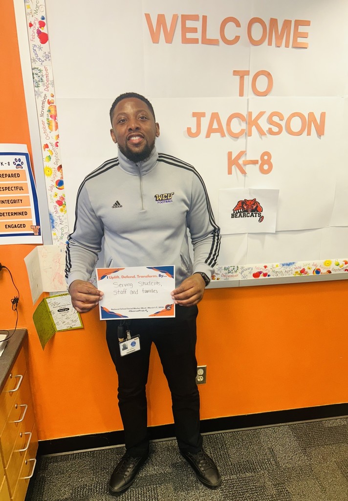 A district staff member is holding a sign that says "I Uplift. Defend. Transform. By... serving students, staff and families."