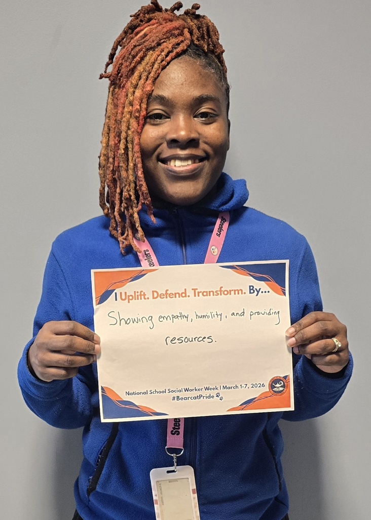 A district staff member is holding a sign that says "I Uplift. Defend. Transform. By... Showing empathy, humility, and providing resources."