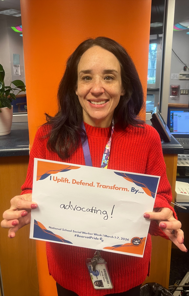 A district staff member is holding a sign that says "I Uplift. Defend. Transform. By... advocating!"