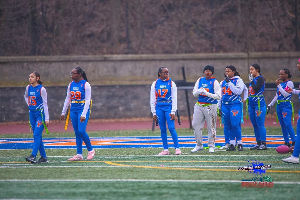 A group of female flag football players are standing on a field. 