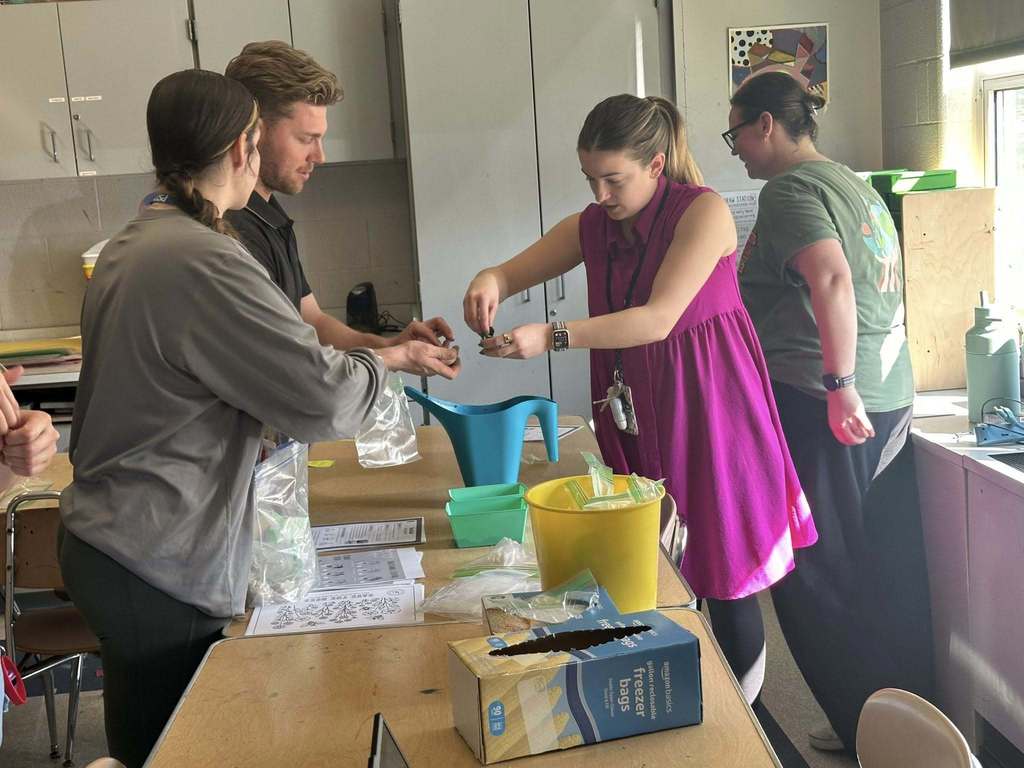 A group of district staff members are gathered around a table with craft supplies in a school classroom. 