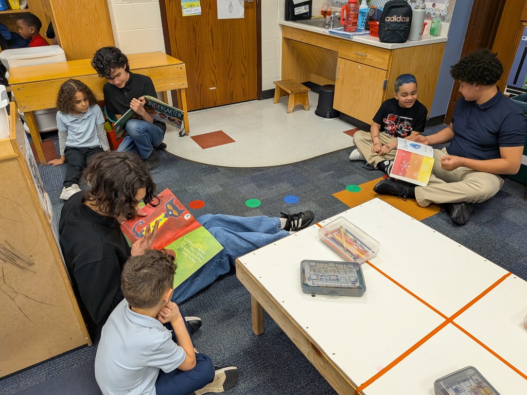 A diverse group of students are seated on the floor in a school classroom, engaging in reading colorful picture books.