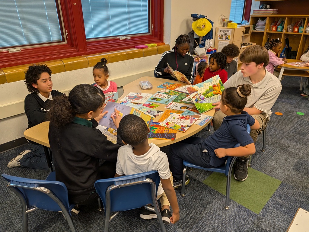 A diverse group of students are seated around a table in a school classroom, engaging in reading colorful picture books.