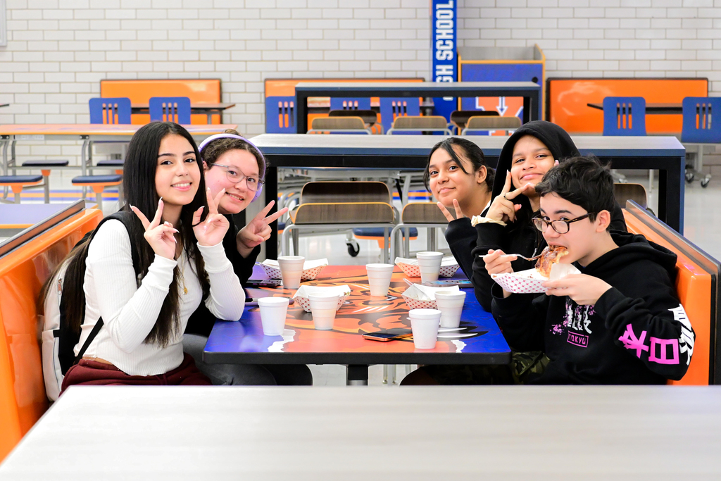 A group of five students are sitting at a table in a school cafeteria enjoying a meal together.