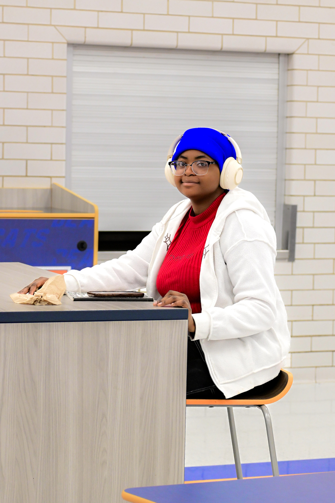 A student wearing headphones is sitting at a table in a school cafeteria.