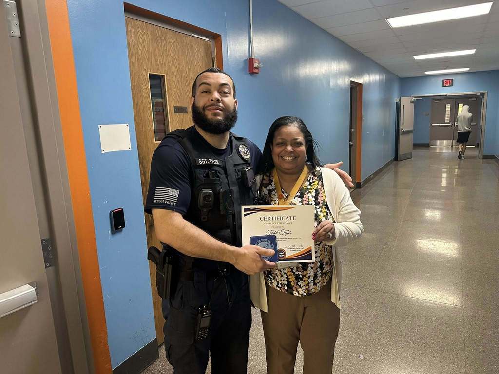Dr. Andrea Berry-Brown, Superintendent of Schools, is standing next to a district staff member who is holding a Perfect Attendance certificate for the second marking period. A student can be seen nearby in the background.