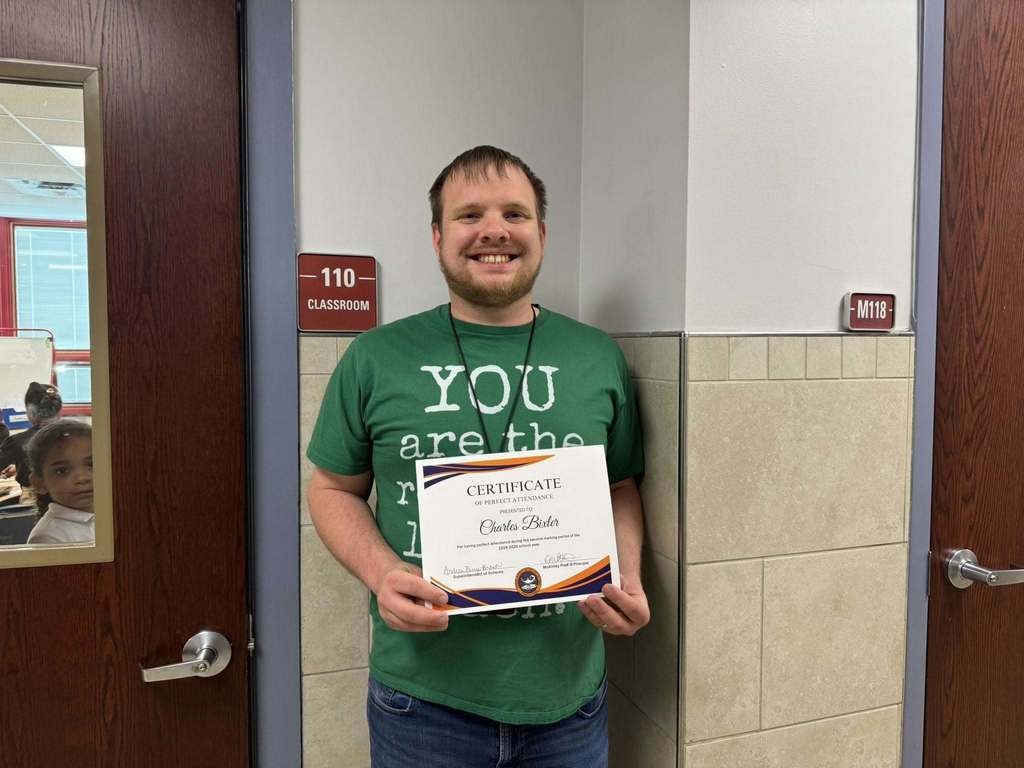 A district staff member is standing near a door, holding a Perfect Attendance certificate for the second marking period.