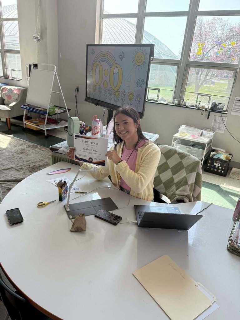 A district staff member is sitting at a table, holding a Perfect Attendance certificate for the second marking period.