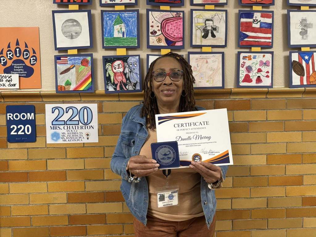 A district staff member is standing in front of a wall, holding a Perfect Attendance certificate for the second marking period.