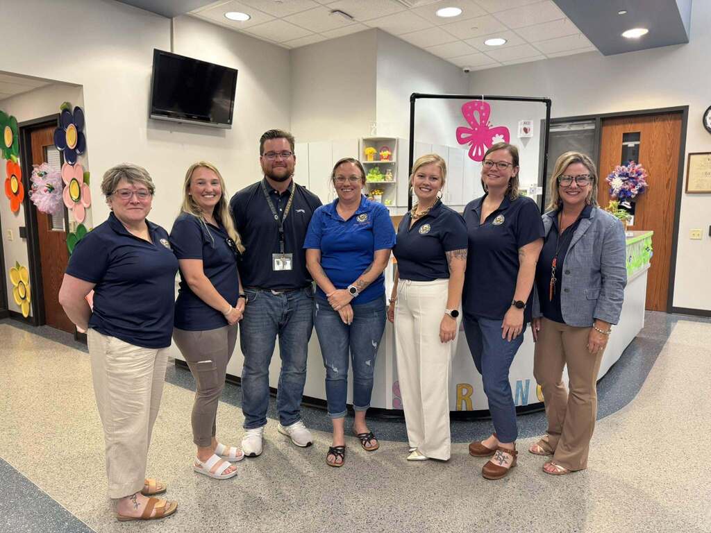 A group of district staff members that are apart of the Office of Academics are posing together in a lobby area.