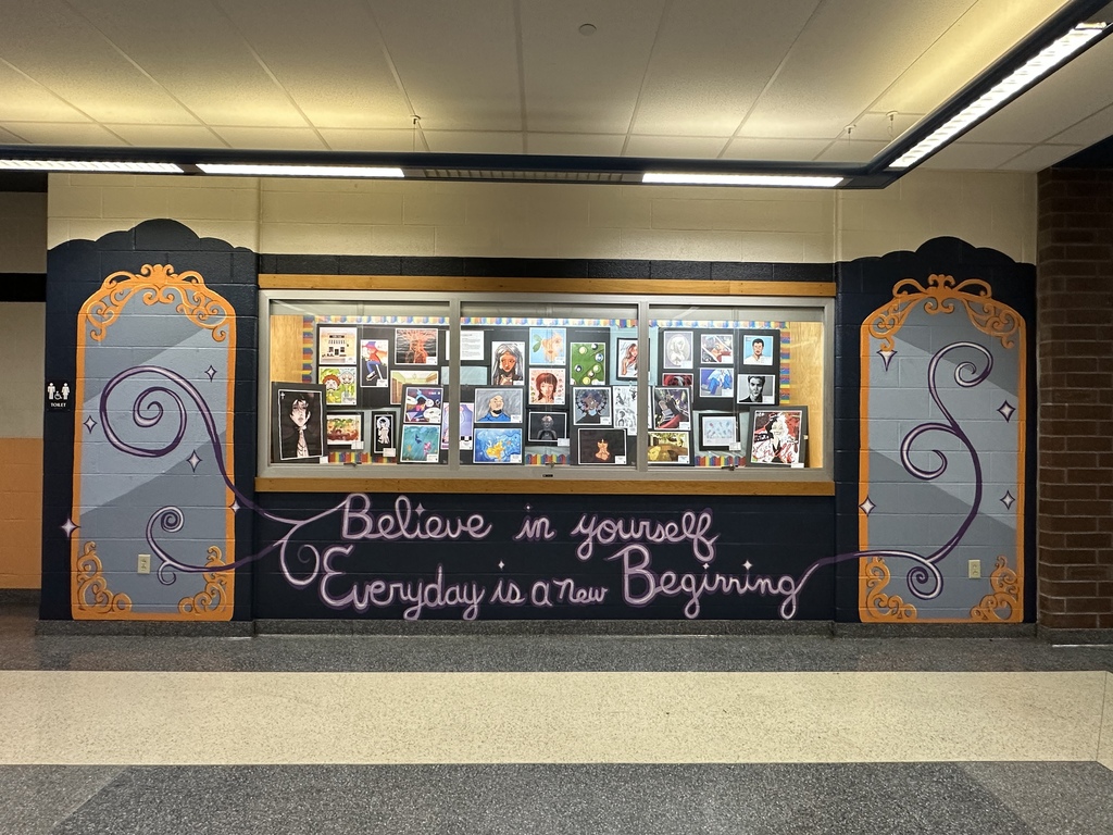 A school hallway mural frames a student art display with decorative mirror designs and the inspirational message, "Believe in yourself. Every day is a new beginning."