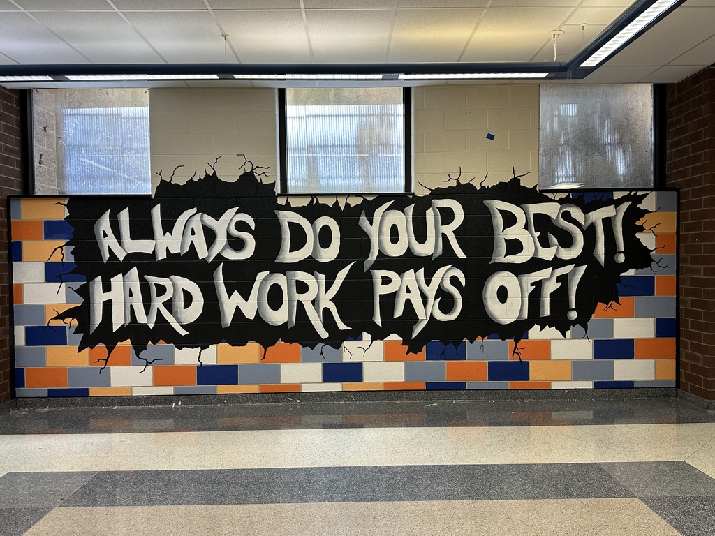 A bold mural in a school hallway displays the message, "Always Do Your Best! Hard Work Pays Off!" in large white lettering on a black background with orange, blue, gray, and white brick accents.