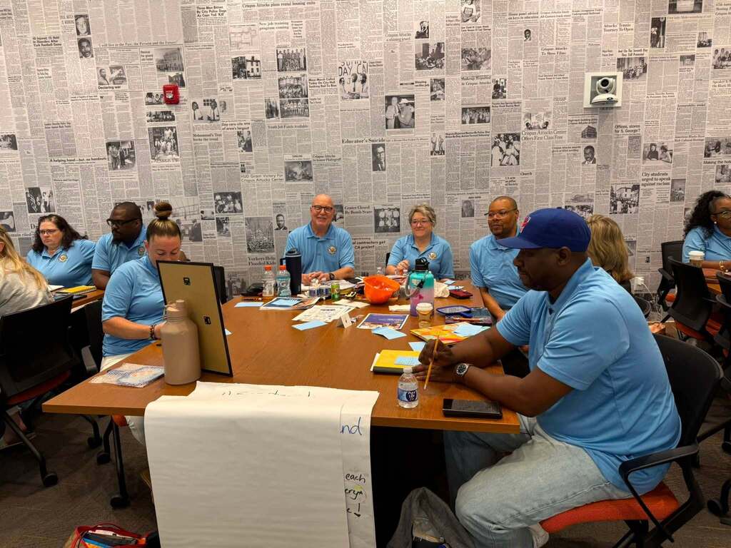 District staff members gather around a table during a professional development session, listening, taking notes, and collaborating.