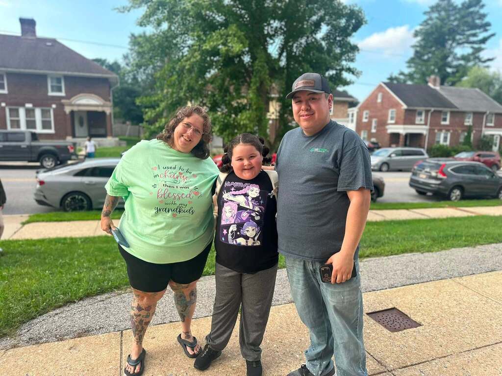 Three family members are posing together outdoors on a sidewalk.