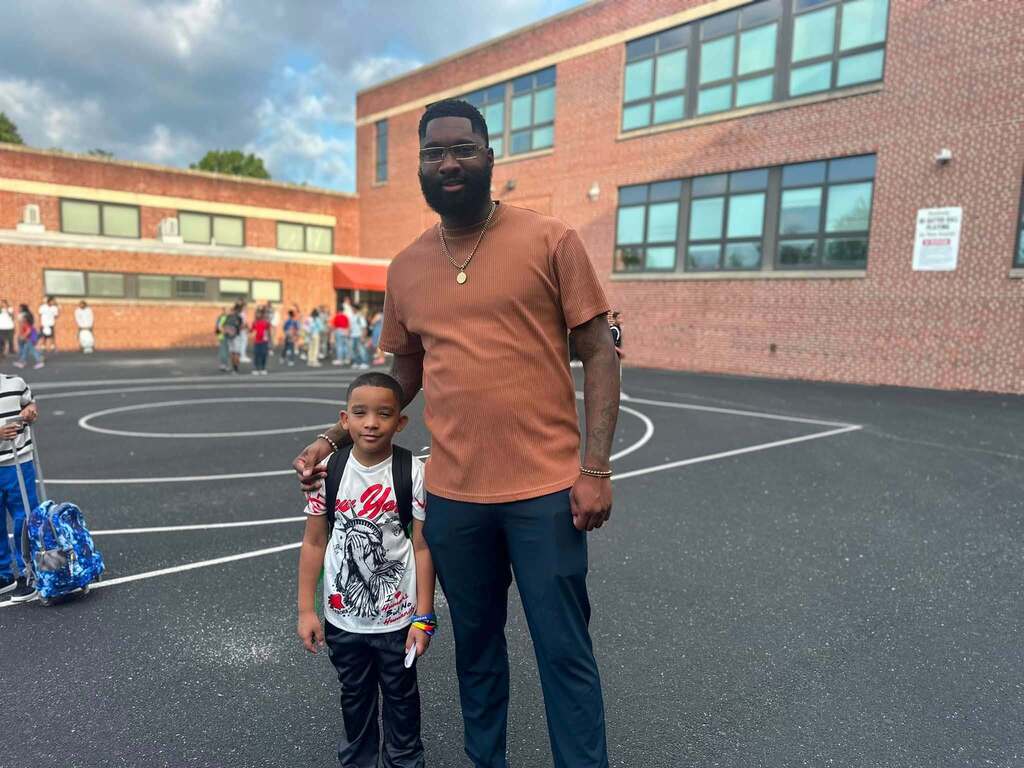 A student and adult are posing together outside a school building.