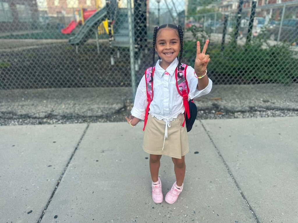 A student is posing outside with a backpack, giving a peace sign.