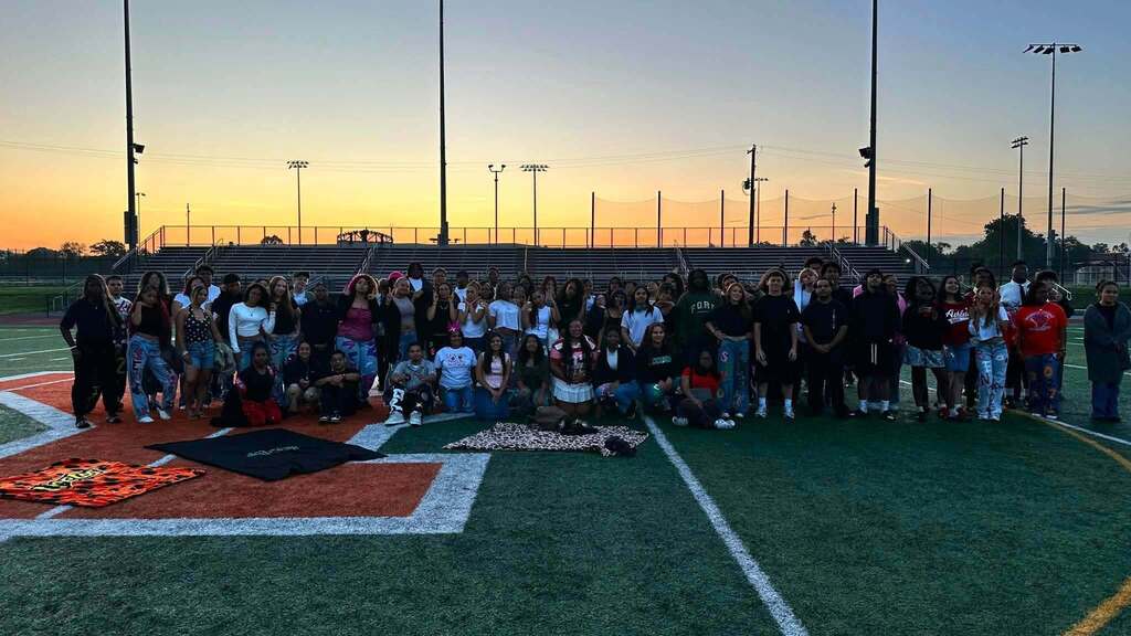 A large group of students are posing together on a football field at sunset.