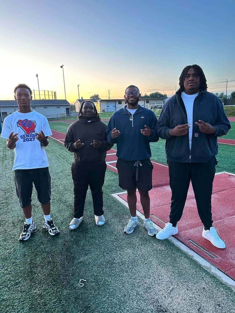 Four students are posing together on a football field at sunrise, with one wearing a Senior 2027 shirt.