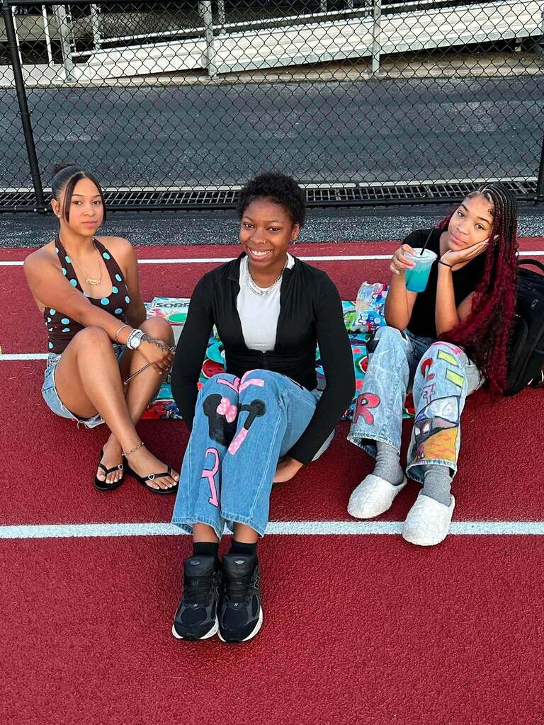 Three students are sitting together on a track, smiling for the camera.