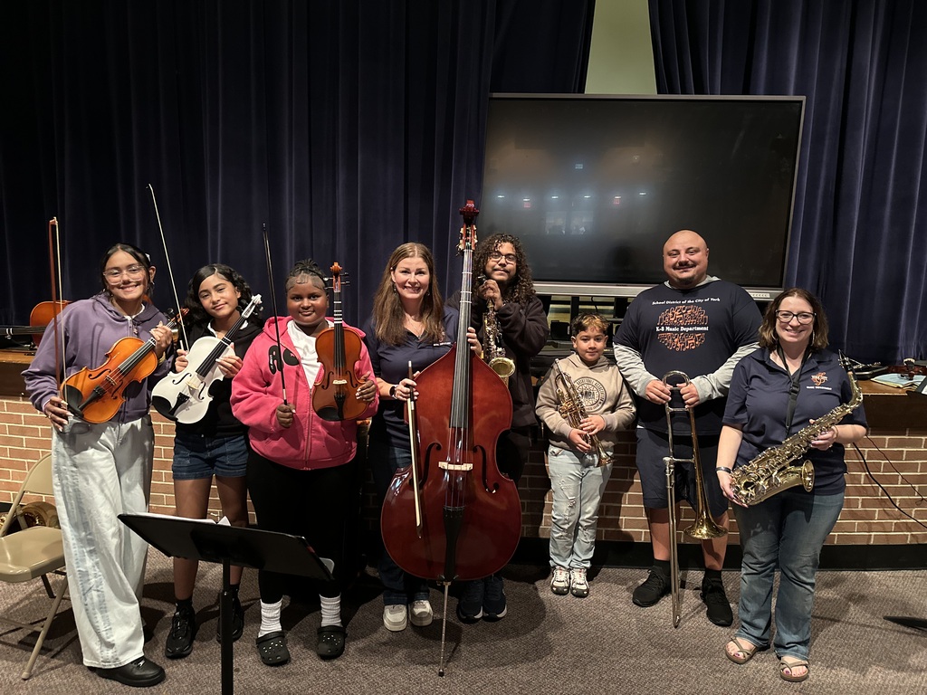 District staff members and students are posing with a variety of musical instruments in a school auditorium.