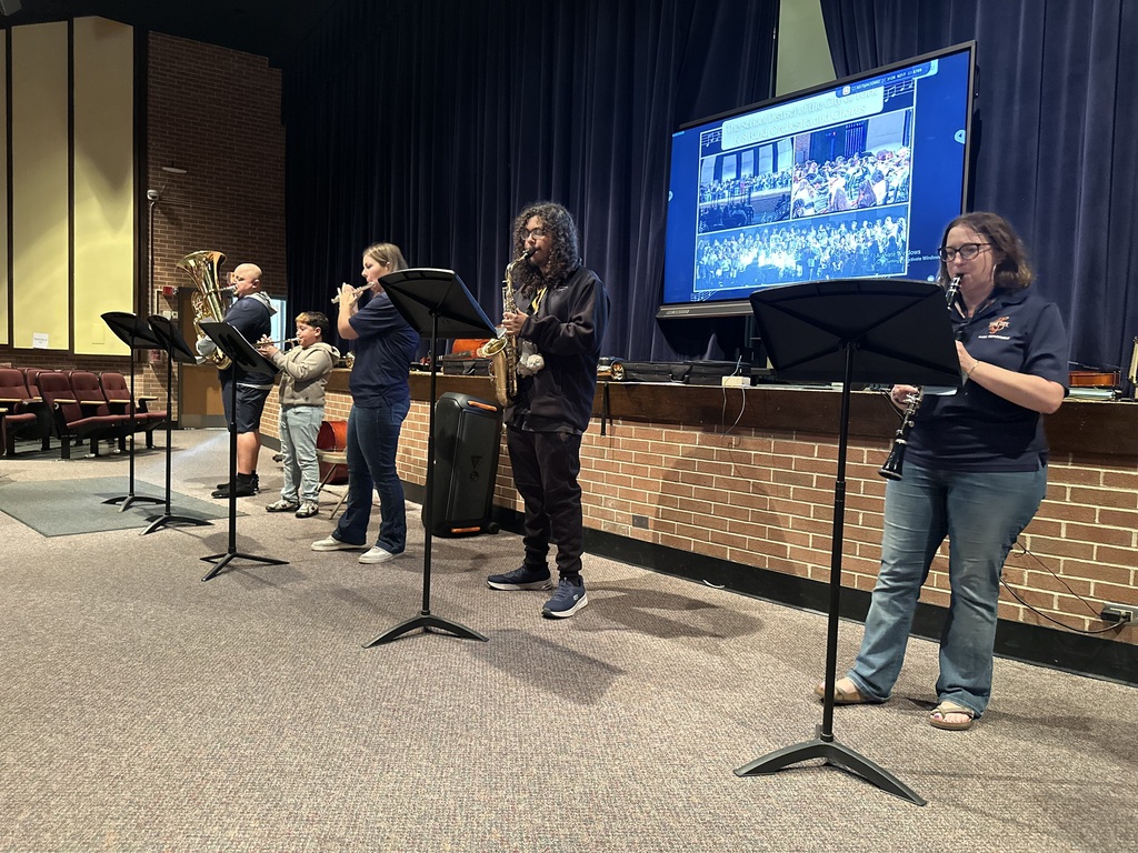 District staff members and students are performing with band instruments in a school auditorium.