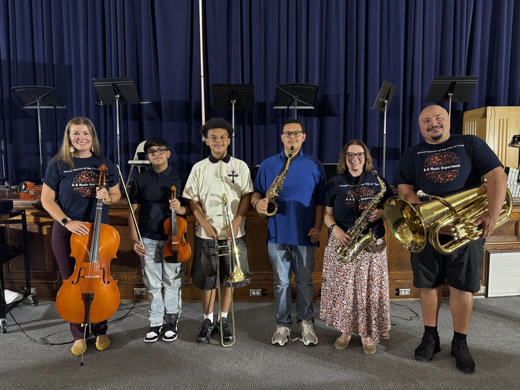 Six district staff members and students are posing with musical instruments on a stage in front of blue curtains.